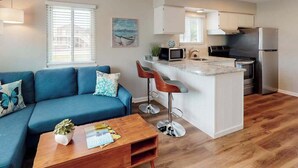 A compact living space with a blue sofa, a coffee table, a kitchen area with a refrigerator, stove, and bar stools. - Al-Be Vacation Villas, Unit 1 (Ocean City)