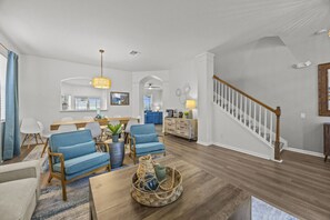 A spacious living room with a wooden floor, a dining area with a long table, blue upholstered chairs, and a staircase with a wooden railing. - Six bedroom  in United States of America, Kissimmee (Kissimmee)