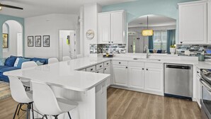 Een moderne keuken met witte kasten, een centraal eiland en een zithoek met een blauwe bank.