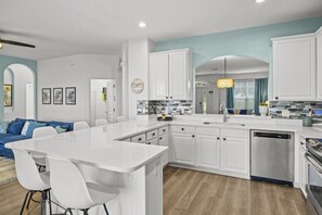 A modern kitchen with white cabinetry, a central island, and a dining area with a blue sofa. - Six bedroom  in United States of America, Kissimmee (Kissimmee)