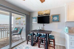 A balcony with a view of the water, a dining area with a table and bar stools, and a TV mounted on the wall. - Renovated bayfront condo with water-view balcony & fast WiFi - walk to beach (Ocean City)