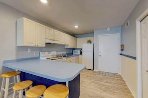 A kitchen with a central island, bar stools, a refrigerator, and a microwave. - Bayside condo with balcony, sunset view, pool & tennis - steps to Jolly Roger (Ocean City)