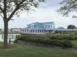A large, two-story building with a blue roof, surrounded by greenery and a body of water. - Harbour Club 5E (Ocean City)