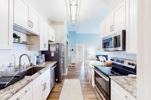 A modern kitchen with white cabinets, a stainless steel refrigerator, a microwave, and a stove. - Harbour Club 5E (Ocean City)