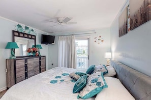 A bedroom with a bed, a ceiling fan, a TV, a dresser, and a balcony with curtains. - Fantastic waterfront escape with furnished deck, WiFi, shared pool & central AC (Ocean City)