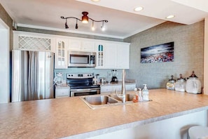 A modern kitchen with white cabinetry, stainless steel appliances, a granite countertop, and a hanging light fixture. - Fantastic waterfront escape with furnished deck, WiFi, shared pool & central AC (Ocean City)