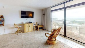 A room with a large window, a flat-screen TV, a wooden desk, a chair, and a bookshelf. - Fountainhead Towers 305 (Ocean City)