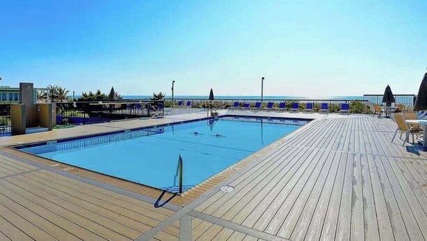 A pool area with a wooden deck, lounge chairs, and a view of the sea. - Fountainhead Towers 305 (Ocean City)