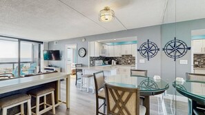 Una cocina moderna con una isla grande, un comedor con mesa de vidrio y vista al océano.