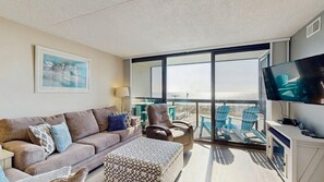 Una sala de estar moderna con un sofá, un sillón, un reposapiés y un televisor sobre un mueble.