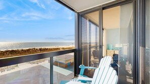 A balcony with a view of the beach and ocean, a glass door, and a chair. - Family-friendly oceanfront condo with balcony, pools, game room & gym (Ocean City)