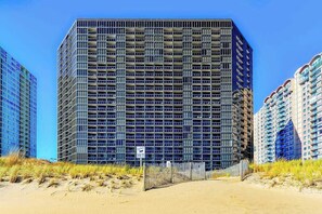 Een hoog gebouw met een raster van ramen, omgeven door duinen en andere gebouwen.