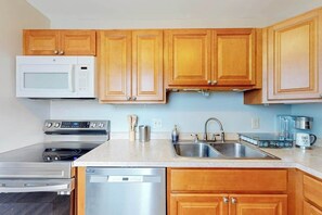 A kitchen with wooden cabinets, a microwave, a stove, a dishwasher, a sink, and a coffee maker. - Captain's Quarters (Ocean City)