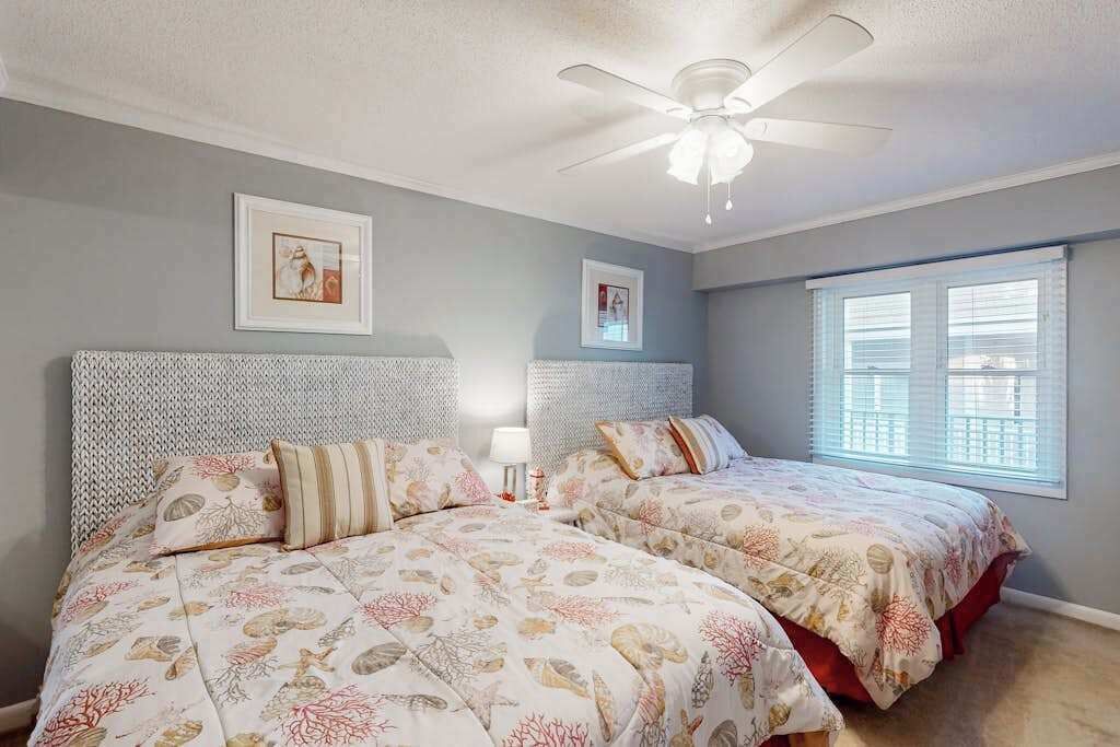 A bedroom with two beds, a ceiling fan, and two framed pictures on the wall.