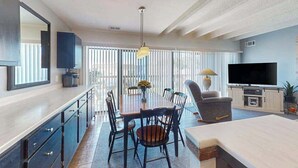 Un salon moderne comprenant un coin repas, un téléviseur à écran plat et une grande fenêtre équipée de stores.