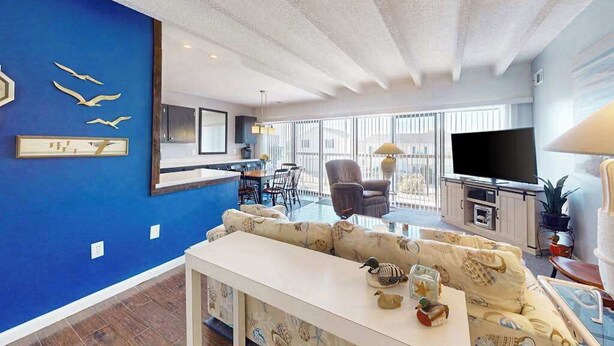 Un salon moderne avec un mur d’accent bleu, un canapé, une table basse, un téléviseur et un coin repas avec des chaises et une table.