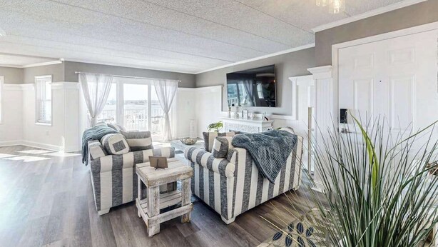 A living room with two striped sofas, a small wooden table, a flat-screen TV, and a large potted plant. - Luxury - bay view condo with balcony, pool, W/D, AC & a short walk to the beach (Ocean City)