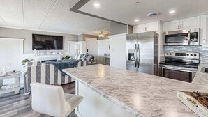 A modern kitchen with a marble countertop, stainless steel appliances, and a seating area with a sofa and chairs. - Luxury - bay view condo with balcony, pool, W/D, AC & a short walk to the beach (Ocean City)