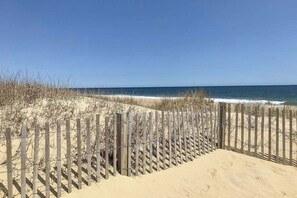 Ein sandiger Strand mit einer Holzumzäunung und einem strahlend blauen Himmel.