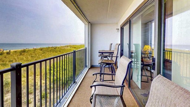 Ein Balkon mit Blick auf den Strand, einem Tisch mit Stühlen und einer Glastür.