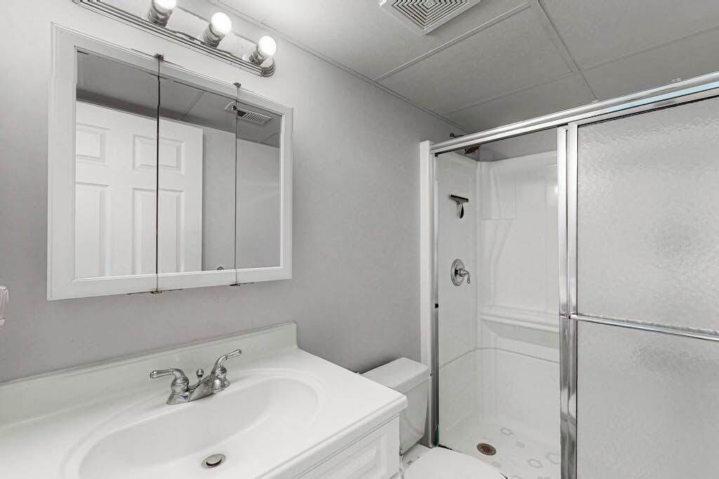 Een badkamer met een witte wastafel, een spiegel en een douche met glazen wanden.