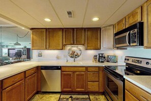 A kitchen with wooden cabinets, a dishwasher, a microwave, and an oven. - Spacious, oceanfront condo with balcony, AC, full kitchen & stunning beach views (Ocean City)