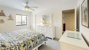 Ein Schlafzimmer mit Bett, Kommode, Spiegel, Deckenventilator und Fenster.