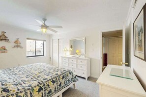 A bedroom with a bed, a dresser, a mirror, a ceiling fan, and a window. - Spacious, oceanfront condo with balcony, AC, full kitchen & stunning beach views (Ocean City)