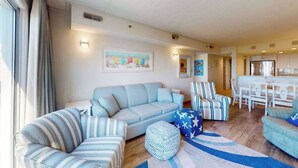 A living room with a sofa, striped chairs, a rug, and a dining area with a table and chairs. - Triton's Trumpet B502 (Ocean City)