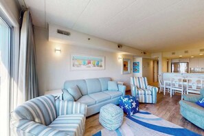 Uma sala de estar com sofá, cadeiras listradas, um tapete e uma área de jantar com mesa e cadeiras.