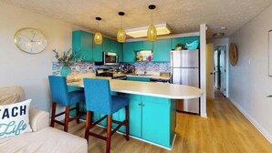 A modern kitchen with teal cabinets, a central island, and pendant lighting. - Bonnie Belle 208 (Ocean City)