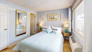 A bedroom with a bed, a mirror, bedside lamps, a window, and a wall-mounted picture. - Bonnie Belle 208 (Ocean City)