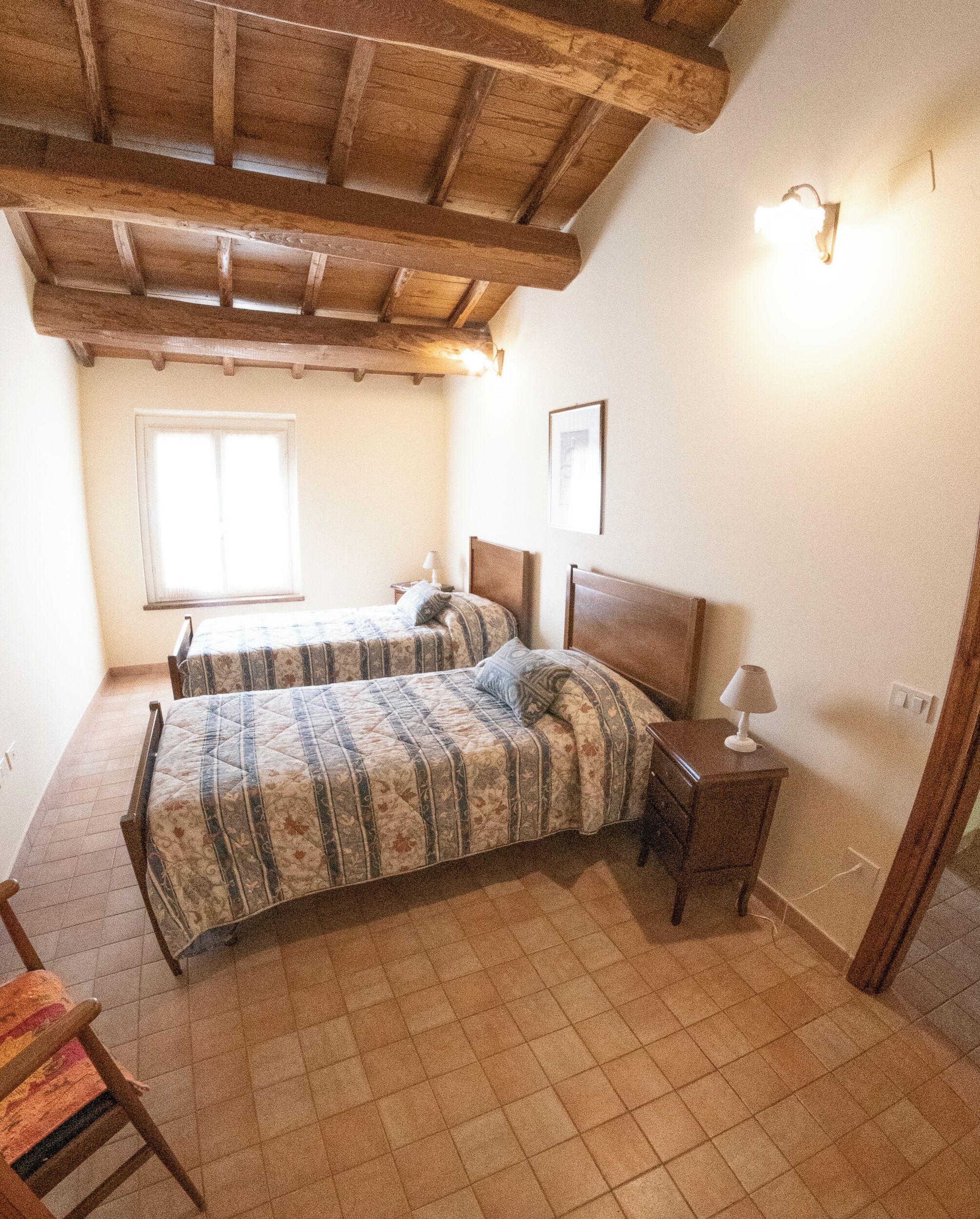 A bedroom with two beds, a window, a nightstand, and a wooden ceiling.