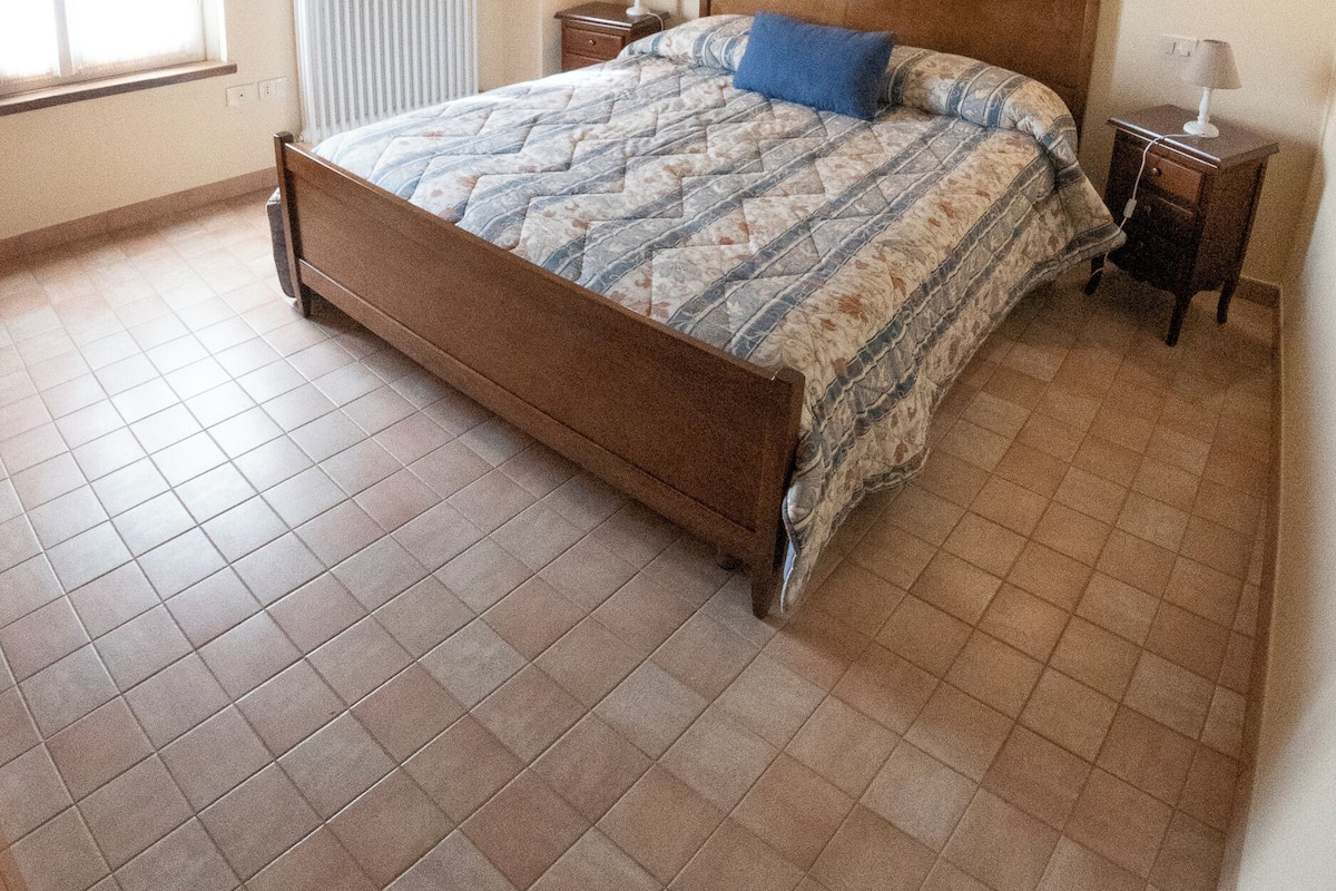 Ein Schlafzimmer mit Holzboden, einem Bett, einem Nachttisch, einer Lampe und einem Heizkörper.