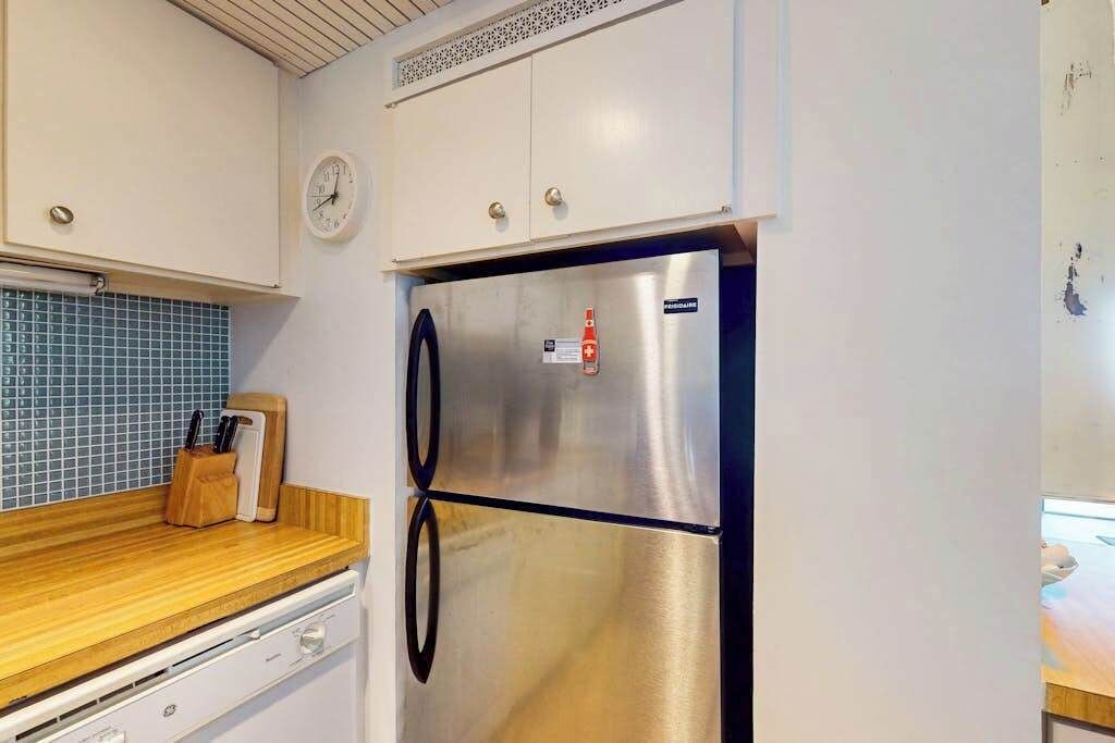 A kitchen with a stainless steel refrigerator, a wooden countertop, and a clock on the wall.