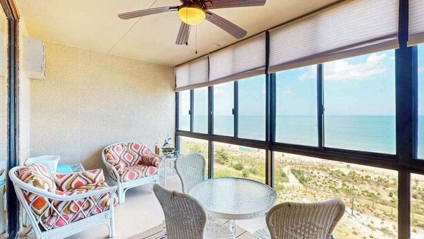 Varanda com móveis de vime, ventilador de teto e vista para a praia.