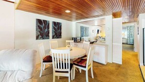 Um interior moderno com teto de madeira, área de jantar com cadeiras brancas e cozinha ao fundo.