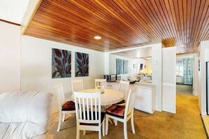 A modern interior with a wooden ceiling, a dining area with white chairs, and a kitchen in the background. - High Point North 6C (Ocean City)