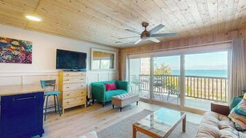 A room with a ceiling fan, a TV, a sofa, a coffee table, and a view of the ocean.