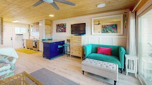 Interior acogedor de una cabaña con techo de madera, un sofá verde, un comedor y una cocina.