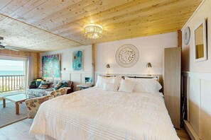 A bedroom with a large bed, a sofa, a chandelier, and artwork on the walls.