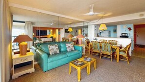 Een woonkamer met een blauwgroene bank, een gele salontafel en rieten stoelen.