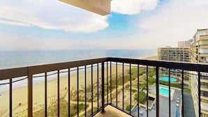 Een balkon met uitzicht op een strand, een zwembad en aangrenzende gebouwen.