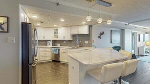 A modern kitchen with white cabinets, a central island, and pendant lighting. - Stunning Ocean front condo w/beach & ocean views, AC & shared pool (Ocean City)