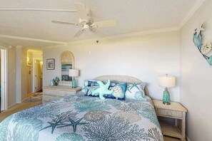 Ein Schlafzimmer mit einem Bett, einem Deckenventilator, einem Nachttisch mit Lampe und einer Wanddekoration.