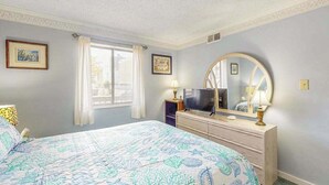 Une chambre à coucher avec un lit, une commode, un téléviseur et un grand miroir.