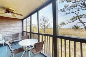 A covered outdoor area with a table and chairs, a ceiling fan, and large windows offering a view of trees and grass. - 1st floor condo w/screened porch kitchen, WiFi Central AC & shared pool (Ocean City)