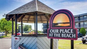 Un kiosque à musique avec une pancarte indiquant la vue sur la plage, un petit kiosque à journaux et, au fond, un immeuble à plusieurs étages.