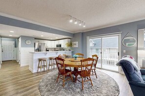 A modern kitchen with white cabinets, a central island, and a dining area with wooden chairs and a rug. - Aventurra 206 (Ocean City)