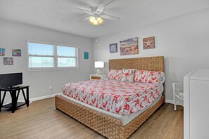 Une chambre à coucher avec un lit, un téléviseur posé sur un meuble, un ventilateur de plafond et des œuvres d’art accrochées aux murs.